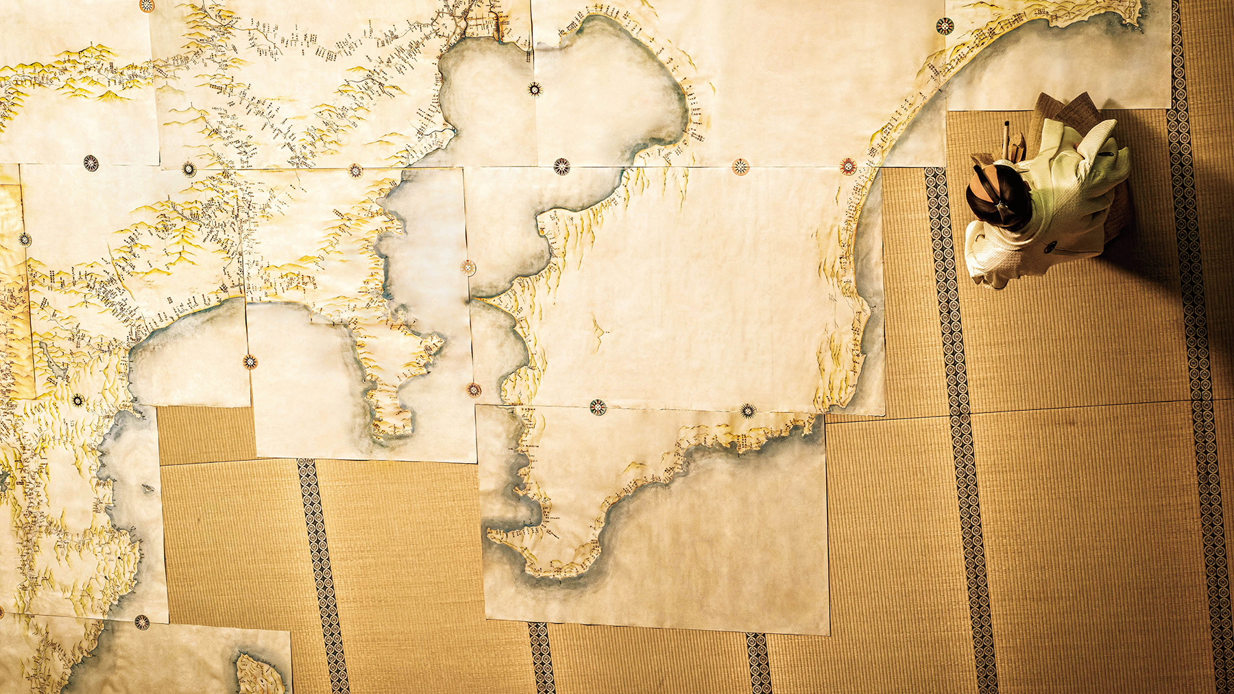 birds eye view of map spread out across floor with man sitting nearby